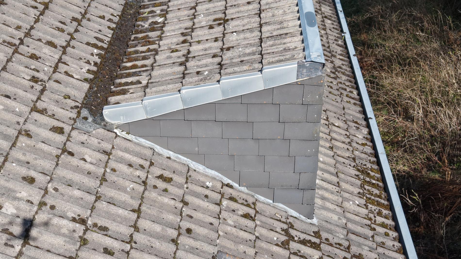 Drohnen-Detailaufnahme eines Gaubenanschlusses: dreieckige Schieferfläche der Gaubenseite trifft auf umliegende Tonziegelfläche, abgedichtet mit einer Bleikehle und Zinkverblechung.